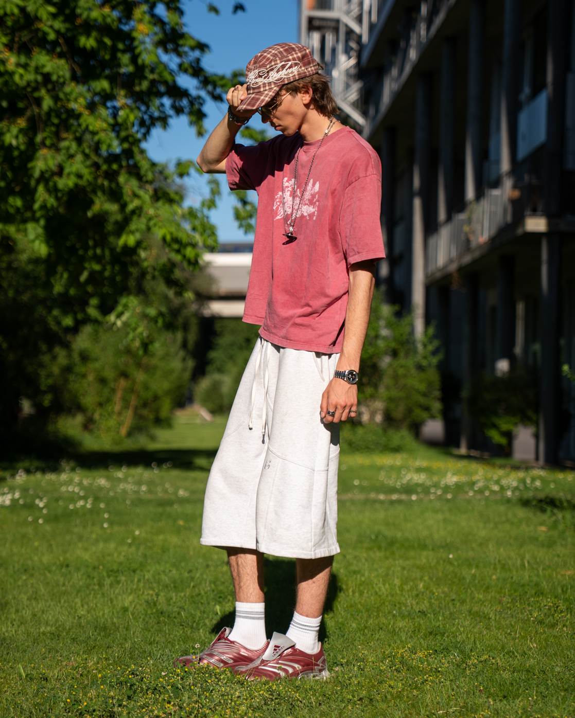 Person wearing a pink shirt and white shorts standing on grass with trees and a building in the background