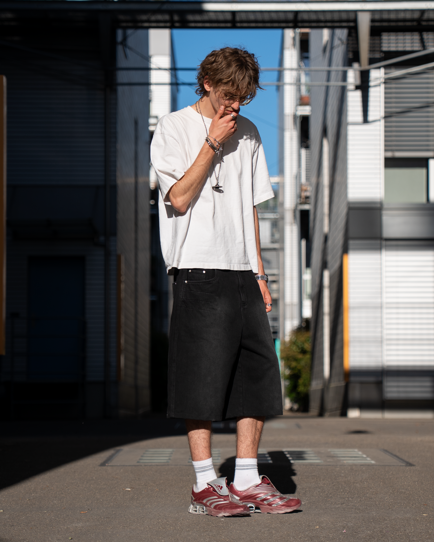 Person standing on a street with a skateboard, wearing a white t-shirt and black shorts.