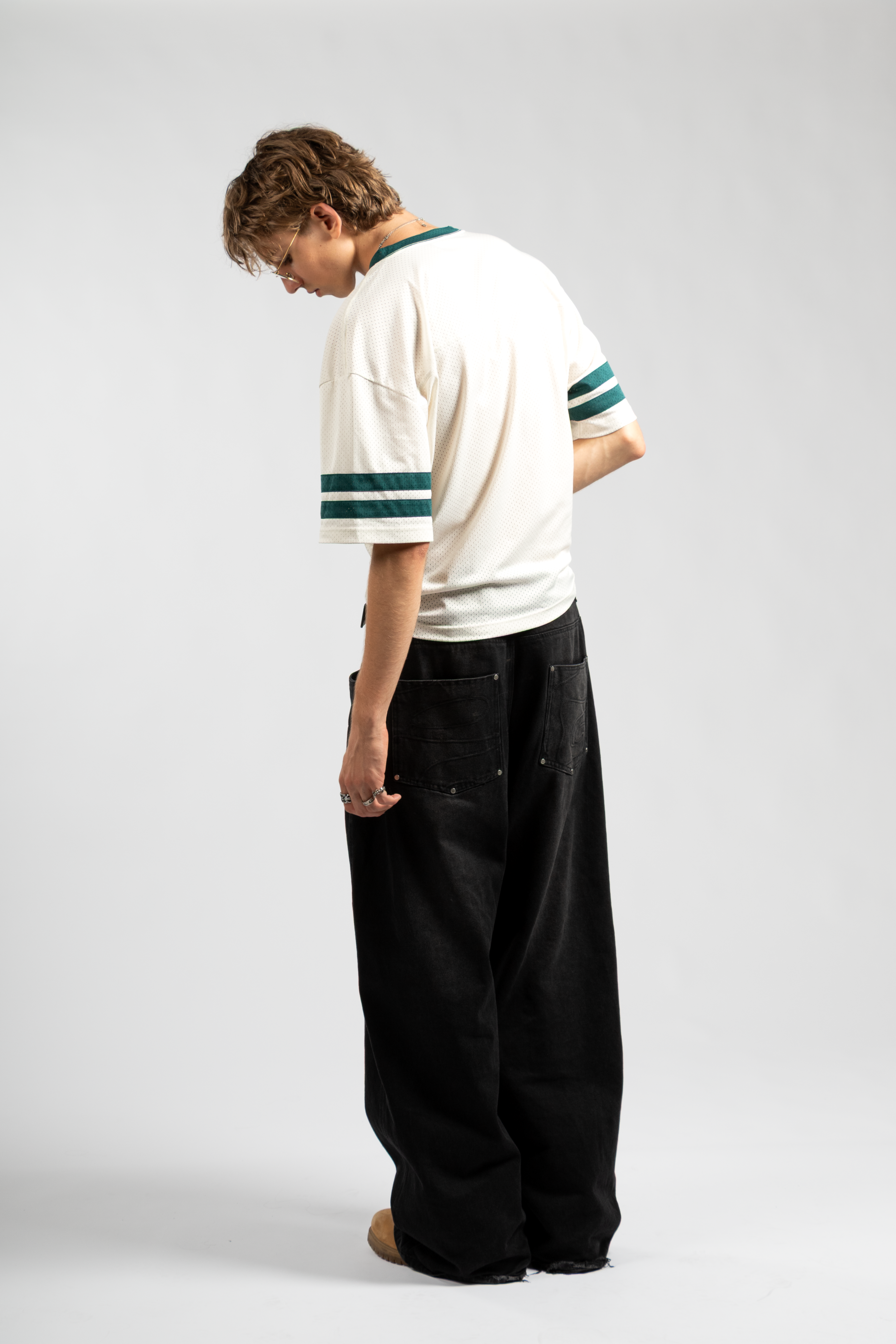 Model wearing oversized black baggy jeans with double back pockets, paired with a loose white jersey tee featuring green stripe details for a retro streetwear look