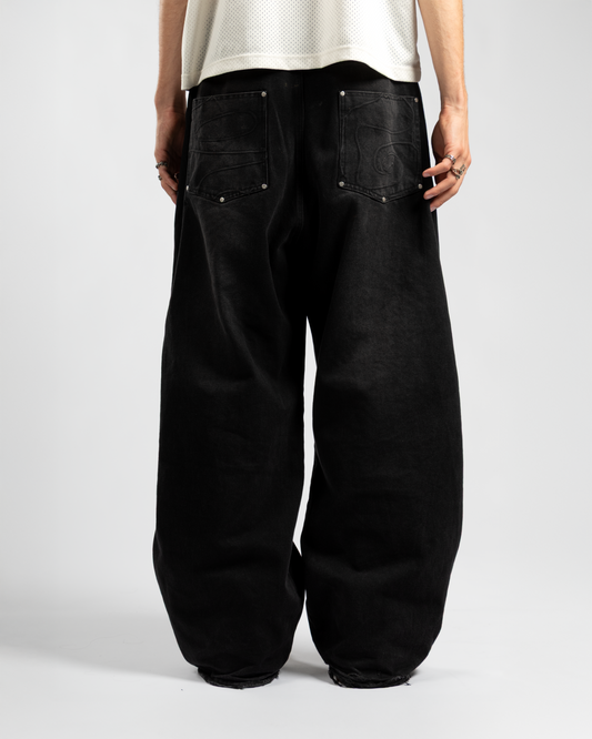 Back view of Whillie Clothing’s oversized black baggy jeans featuring tonal swirl embroidery on both pockets and extra-wide leg fit, styled with a mesh jersey for a relaxed streetwear aesthetic
